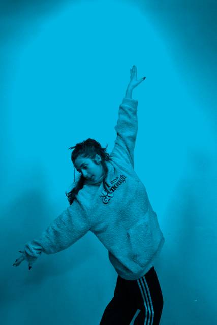 Una joven baila con entusiasmo en un fondo azul.