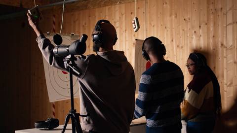 Un grupo de personas practica en un campo de tiro con dianas en la pared.