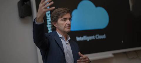 Un hombre está presentando con entusiasmo frente a una pantalla que muestra un logo de nube.