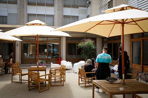 Un patio con mesas y sombrillas donde varias personas conversan y se relajan.