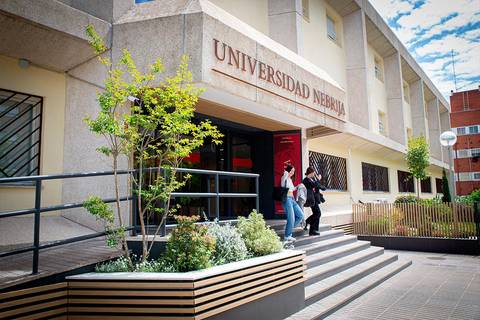 La imagen muestra la entrada de la Universidad Nebrija con estudiantes saliendo del edificio.