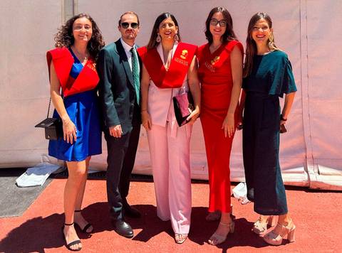 Un grupo de cinco personas posando en un evento, todas vestidas elegantemente y con sashes de celebración.
