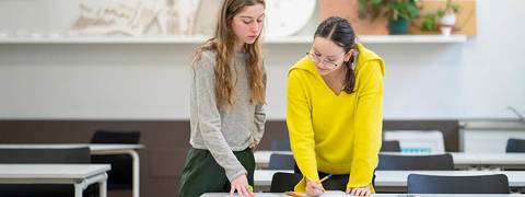 Dos mujeres colaboran en un trabajo en un aula moderna.
