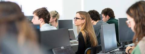 Un grupo de estudiantes en un aula frente a computadoras.