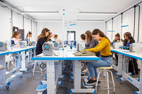 Un grupo de mujeres jóvenes trabaja en máquinas de coser en un taller de costura.