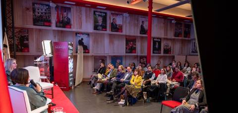 Una conferencia o evento con un público atento en un salón decorado con carteles en las paredes.