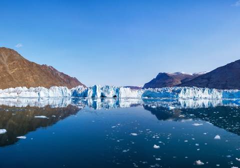Una vista panorámica de un glaciar reflejándose en aguas tranquilas bajo un cielo despejado.