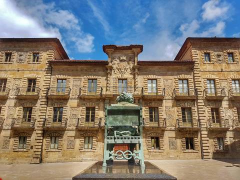 Una imagen de un edificio antiguo con un monumento en el centro y un cielo parcialmente nublado.