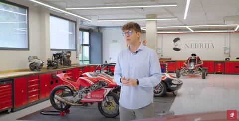 Un joven presenta un taller de automóviles con coches de carreras y motores a la vista.