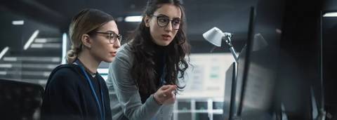 Dos mujeres trabajadoras colaboran frente a una computadora en un entorno moderno y tecnológico.