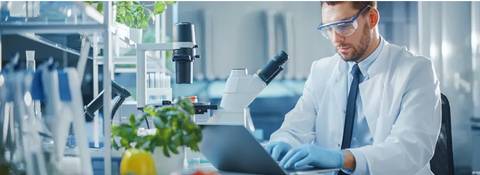 Un científico trabaja en un laboratorio utilizando un microscopio y una computadora.