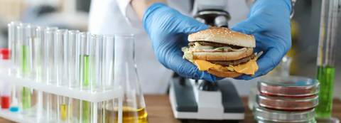 Un científico sostiene una hamburguesa frente a un microscopio en un laboratorio.