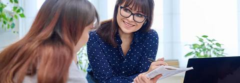 Dos mujeres conversan y toman notas en un ambiente de trabajo.