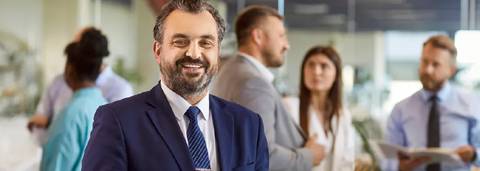 Un grupo de profesionales conversando en un ambiente de oficina, con un hombre al frente sonriendo.
