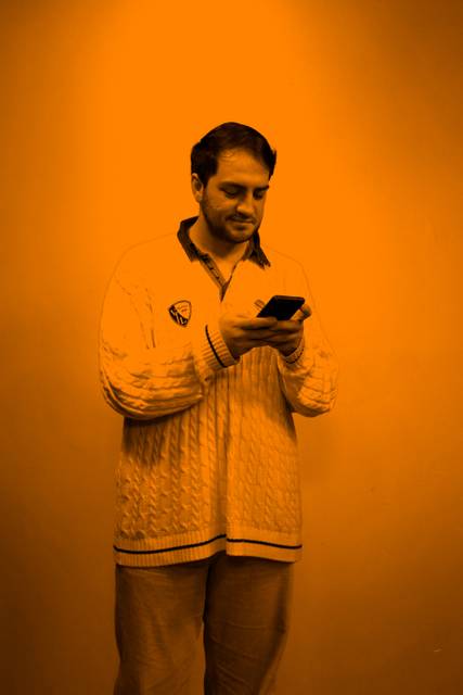 Un hombre con un suéter blanco está mirando su teléfono móvil contra un fondo naranja.