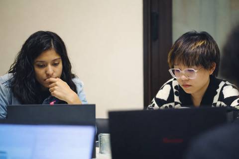 Dos mujeres concentradas en sus computadoras portátiles en un entorno de trabajo colaborativo.