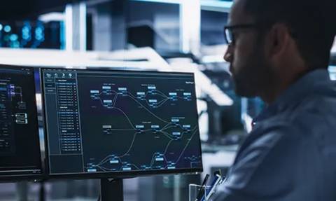 Un hombre trabajando en un ordenador frente a pantallas que muestran gráficos y datos tecnológicos.