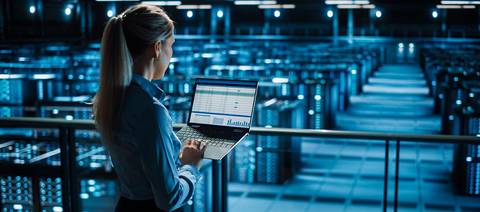 Una mujer observa datos desde una computadora portátil en un centro de datos iluminado en azul.