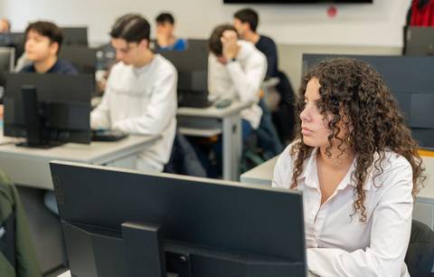 Estudiantes en un aula de clases trabajando en computadoras.