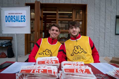 Dos jóvenes con chalecos amarillos sonríen mientras se encuentran en un mostrador de registro en un evento.