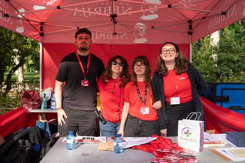 Un grupo de cuatro personas posando sonrientes en un stand al aire libre con un toldo rojo.