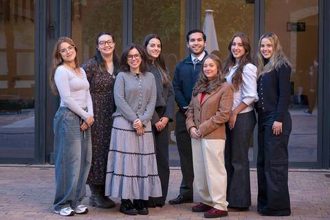 Un grupo de ocho personas posando frente a una entrada con grandes ventanales.