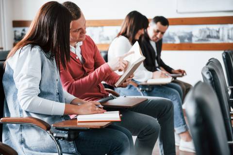 Un grupo de personas sentadas en un aula, concentradas en sus libros y cuadernos.