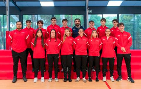 Un grupo de jóvenes atletas posan en un gimnasio, todos vistiendo uniformes rojos con blanco.