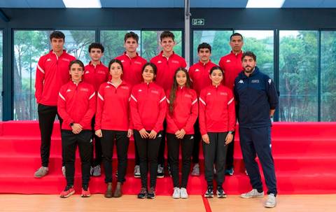 Un grupo de jóvenes atletas posan en un ambiente deportivo, todos vestidos con chaquetas rojas.