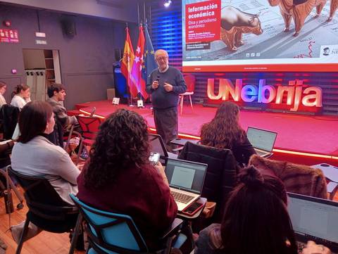 Un profesor habla frente a un grupo de estudiantes durante una clase sobre información económica.