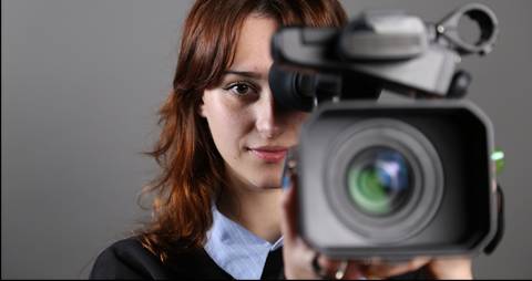 Una mujer sostiene una cámara de video frente a ella con una mirada decidida.