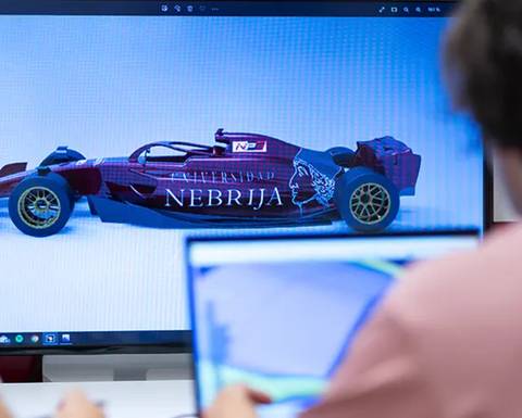 La imagen muestra un auto de carreras con diseño personalizado en la pantalla de una computadora mientras una persona trabaja en otra laptop.