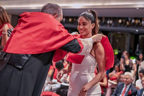 Una mujer sonriente recibe una banda en una ceremonia de graduación.