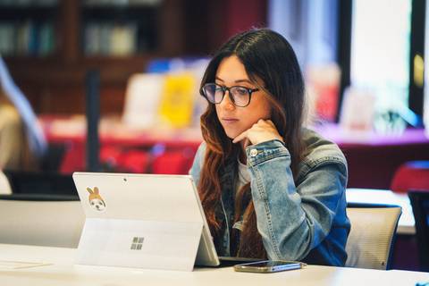 Una mujer con gafas utiliza una tablet mientras está sentada en una mesa.