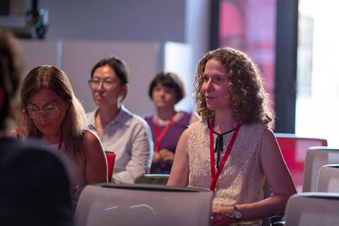 Un grupo de mujeres sentadas en un evento, prestando atención mientras uno de ellas parece estar escuchando atentamente.