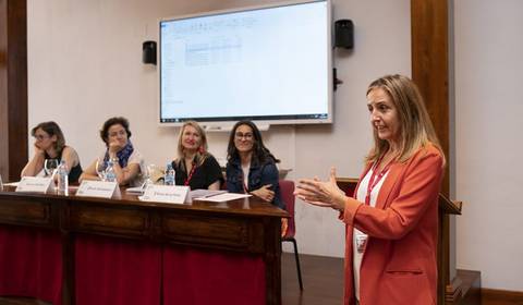 Una mujer habla frente a un grupo de mujeres sentadas en una conferencia.