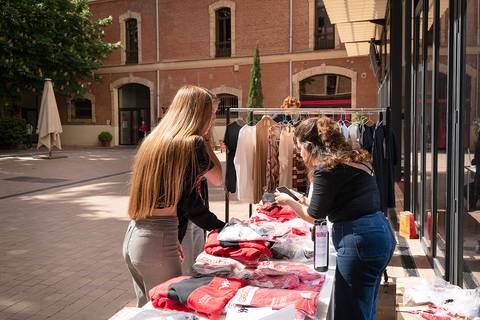 Dos mujeres revisan ropa expuesta en un mercado al aire libre.