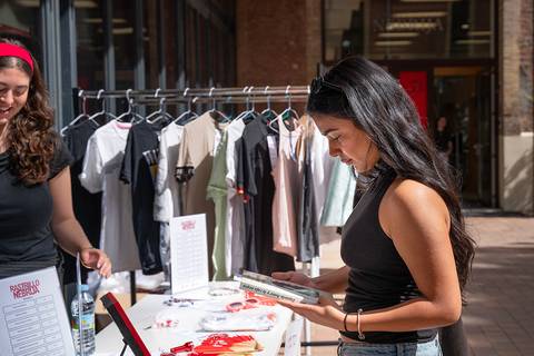Dos jóvenes están en un mercado disfrutando de una venta de ropa y accesorios.