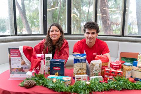Dos personas jóvenes se encuentran sentadas frente a una mesa decorada, rodeados de alimentos y productos de despensa en un entorno festivo.