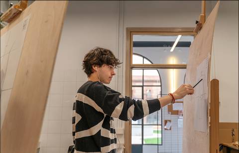 Un joven está dibujando en una hoja de papel en un entorno artístico.