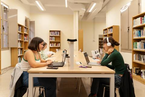 Estudiantes trabajando en un espacio de estudio con laptops en una biblioteca.