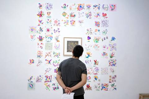 Una persona observa una exhibición de arte con numerosas obras coloridas en una pared blanca.
