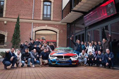 Un grupo de personas sonrientes se reúne frente a un coche de carreras en un evento.
