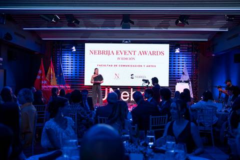 Una ceremonia de premios con asistentes elegantes y una presentación en pantallas al fondo.