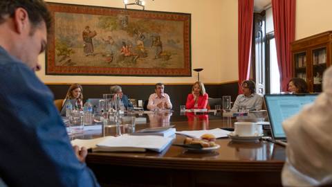 Reunión en una sala con un mural decorativo y varias personas discutendo alrededor de una mesa.