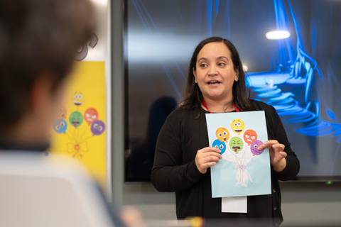 Una mujer está presentando una hoja con dibujos de caras y globos en una sala de clases.