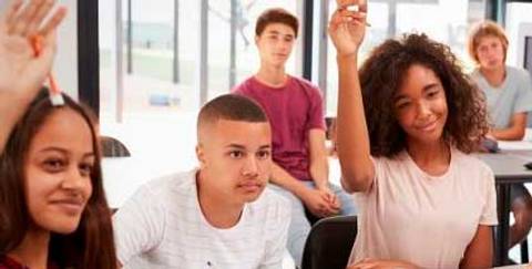 Un grupo de estudiantes en un aula levantando la mano para participar.