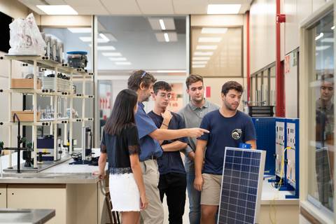 Un grupo de estudiantes observa y discute sobre un panel solar en un laboratorio.
