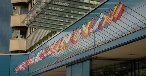 La imagen muestra una fila de banderas de diferentes países colgadas en una edificación moderna.
