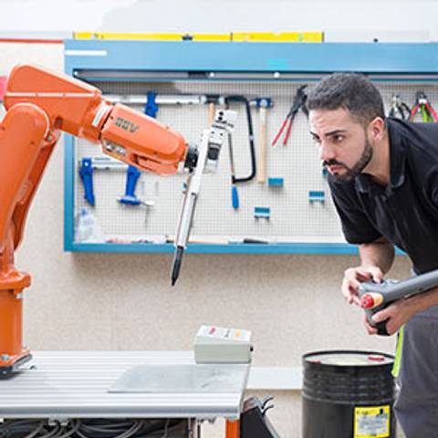 Un hombre observa un robot industrial mientras sostiene herramientas en un entorno de trabajo.